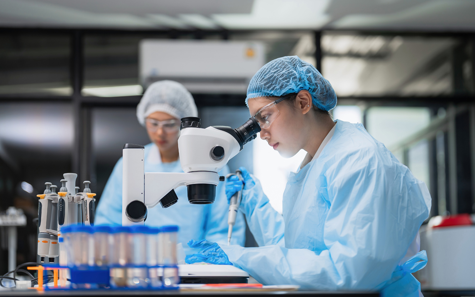 Asian female scientists team using a microscope and a pipette in a laboratory.